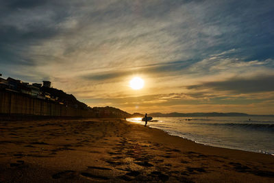 Scenic view of beach with silhouette people against sky during sunrise