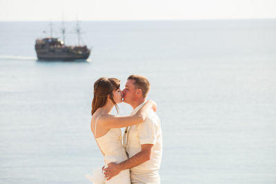Side view of couple embracing against sea