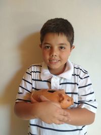 Portrait of boy holding piggy bank against white wall