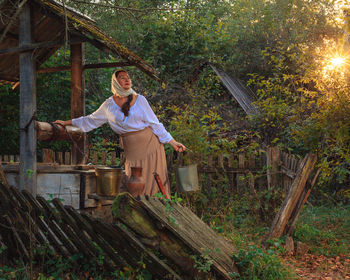 Side view of young woman standing by tree trunk