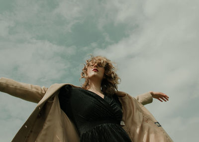 Low angle portrait of woman standing against cloudy sky