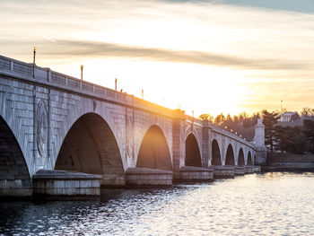 Arch bridge over river during sunset