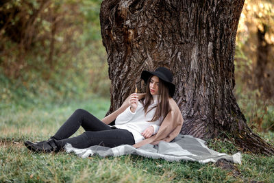 Young woman sitting by tree trunk at park