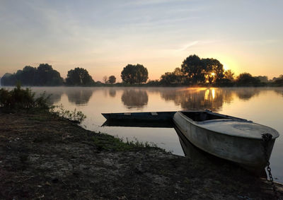 Boat moored in lake against sky during sunset