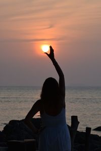 Rear view of woman sitting on beach against sky during sunset