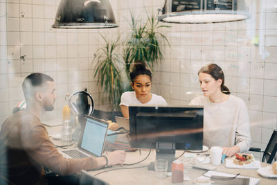 Young multi-ethnic computer programmers discussing at creative office seen through window