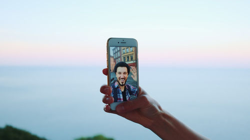 Low angle view of hand using mobile phone against sky