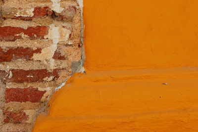 Detail of orange bricks exposed in a yellow painted wall