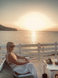 Portrait of woman sitting at beach against sky during sunset