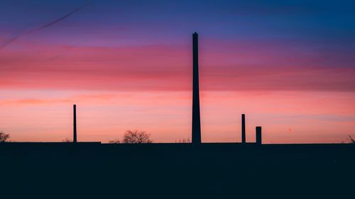 Silhouette of factory against sky during sunset