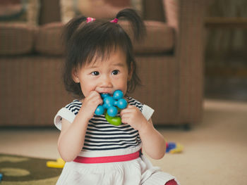 Cute girl biting toy while sitting at home