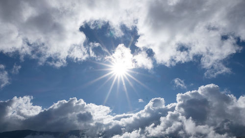 Low angle view of sunlight streaming through clouds