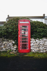 Red telephone booth by wall against sky