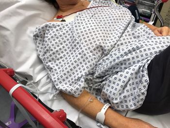 Midsection of woman with iv drip lying on bed in hospital