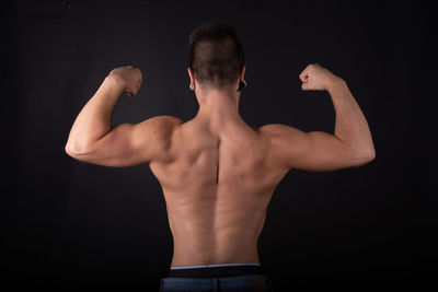 Rear view of shirtless man standing against black background