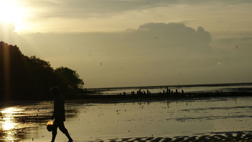 Silhouette man walking on beach against sky during sunset