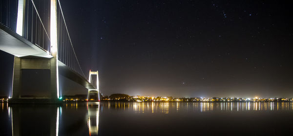 Illuminated bridge over river against sky at night