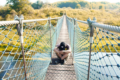 Rear view of man sitting on bridge