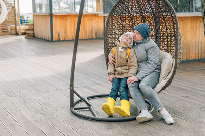 Grandmother and granddaughter sat down to rest after a walk in a hanging rattan chair outdoors