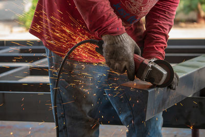 Midsection of man grinding metal at factory