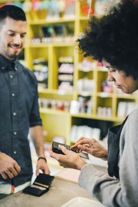 Barista using credit card reader while customer standing in front at cafe