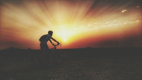 Man riding bicycle on dirt road against sky during sunset