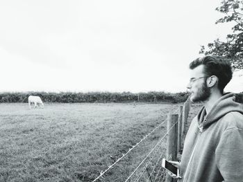 Side view of young man looking away on field against sky