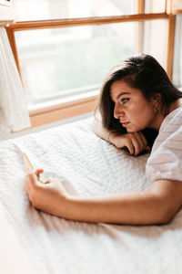 High angle view of young woman using phone while lying on bed at home