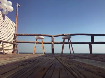 Stools on pier against clear blue sky