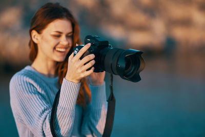 Young woman holding camera while standing outdoors