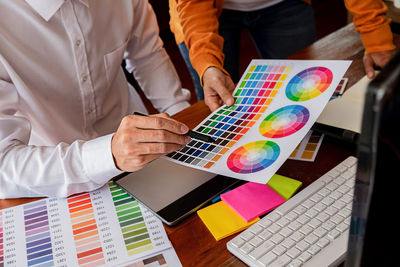 Midsection of creative business people discussing over color swatch at desk in office