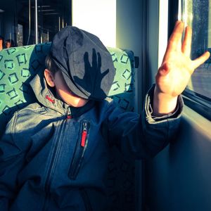 Boy with cap on face gesturing while sitting in train