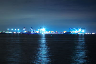 Illuminated city by sea against sky at night