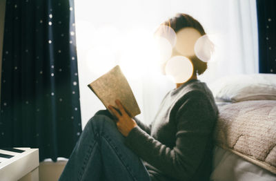 Side view of woman reading book at home
