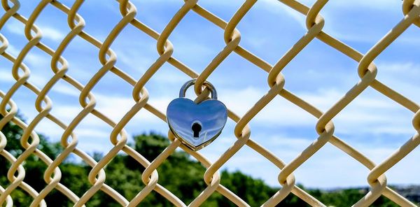 Close-up of padlock on chainlink fence against sky