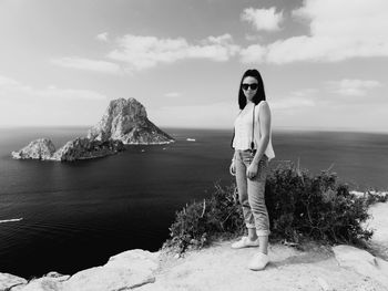 Portrait of young woman standing on rock by sea against sky