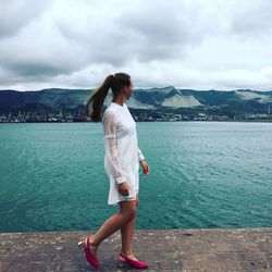 Full length of young woman walking on pier against cloudy sky