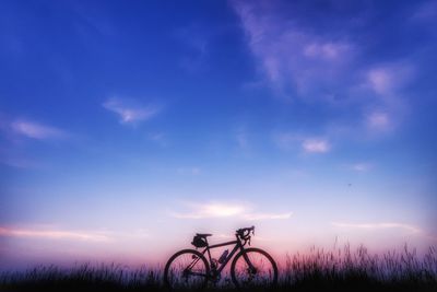 Silhouette bicycle on field against sky at sunset