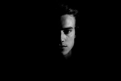 Close-up portrait of a serious young man over black background