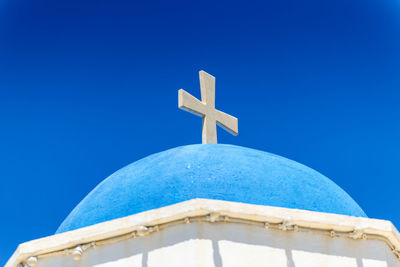 Low angle view of cross on building against clear blue sky