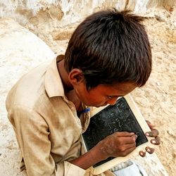 High angle view of boy writing in slate