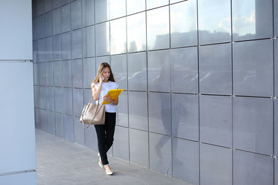 Young businesswoman talking on mobile phone while standing by wall