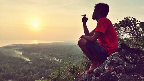 Side view of man smoking cigarette while sitting on mountain