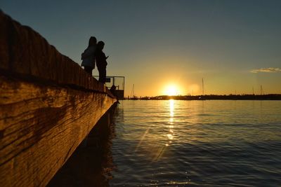 Friends standing on retaining wall by river during sunset