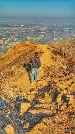 Rear view of man walking on cliff against cityscape