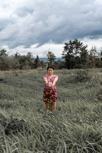 Portrait of young woman standing on field against sky