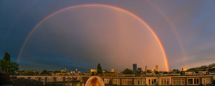Rainbow over city against sky during sunset