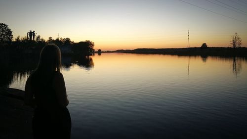 Silhouette woman looking at lake against sky during sunset