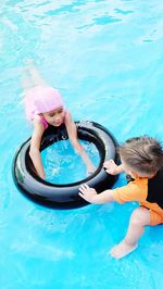 High angle view of siblings with inflatable ring enjoying in swimming pool