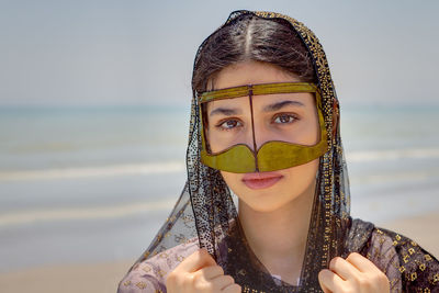 Close-up portrait of young woman wearing traditional clothing standing at beach against sky